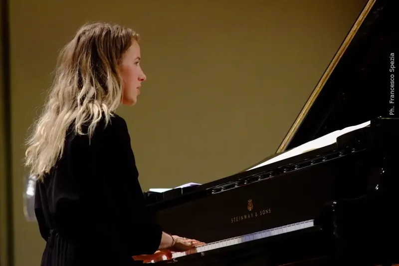 Alexandra Tchernakova in profile, dressed in black, playing a grand piano