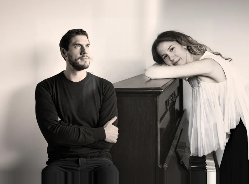 Baritone Leonardo Cremona and Alexandra Tchernakova, both smiling: he on the left, she leaning on the piano on the right