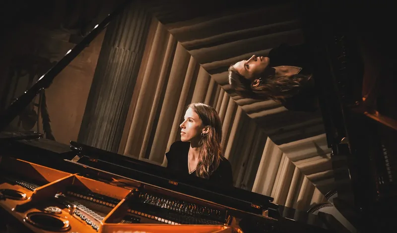 Alexandra Tchernakova playing a grand piano, her face reflected in the raised lid