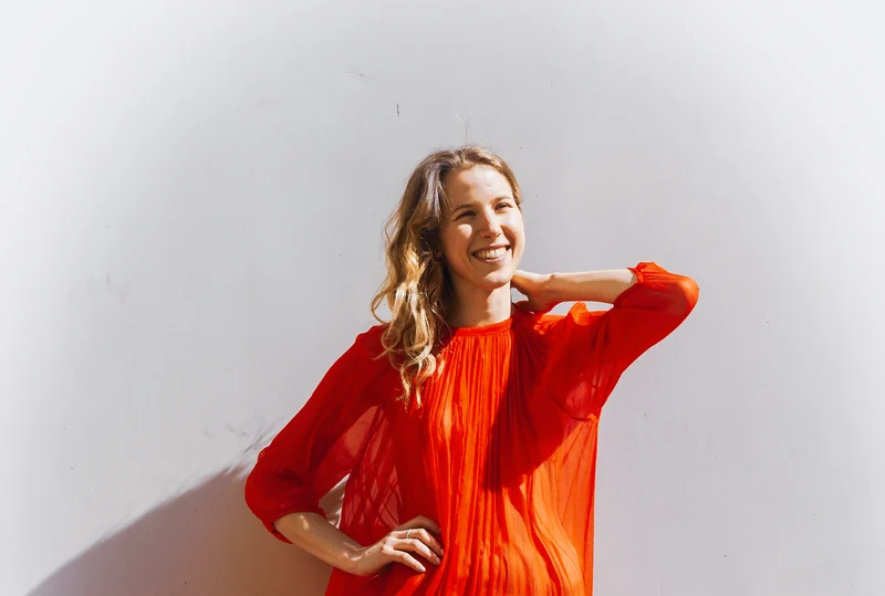 Alexandra Tchernakova laughing in a red dress against a sunlit wall